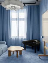 AVOLT office lounge with blue curtains, textured sofa, black sculptural armchair and low wooden coffee table