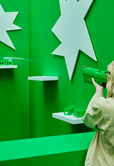 Person aiming AVOLT green handheld blaster at white star targets on vivid green play-wall